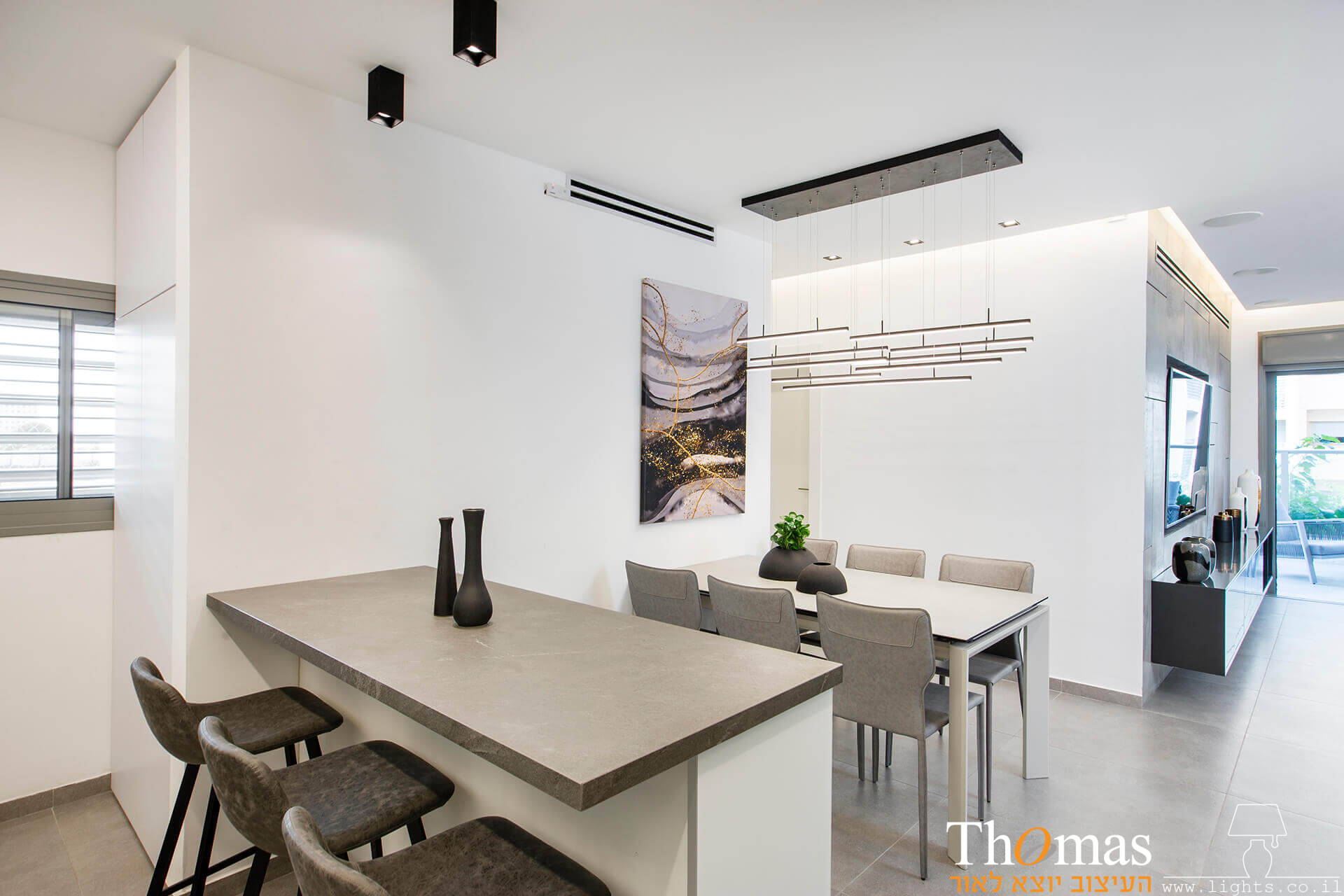 מנורה תלויה מעל פינת אוכל ושתי מנורות צמודות תקרה צילינדרים מעל דלפק במטבח