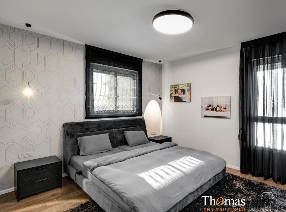חדר שינה בגוונים של אפור ושחור עם תאורה צמודת תקרה ושתי מנורות קריאה תלויות לצד המיטה