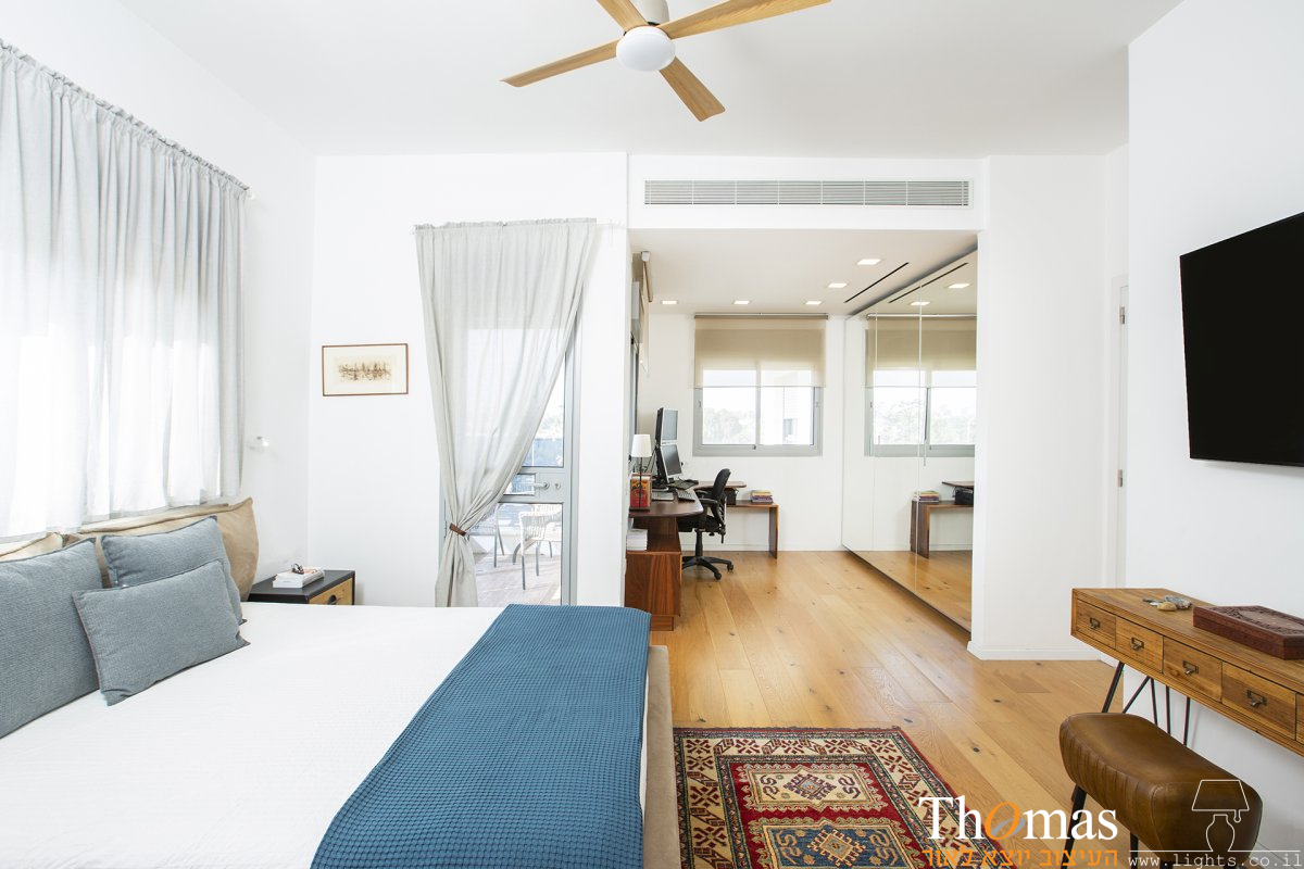 חדר שינה עם מאוורר תקרה מעץ ופינת עבודה מוארת בשקועים מרובעים לבנים